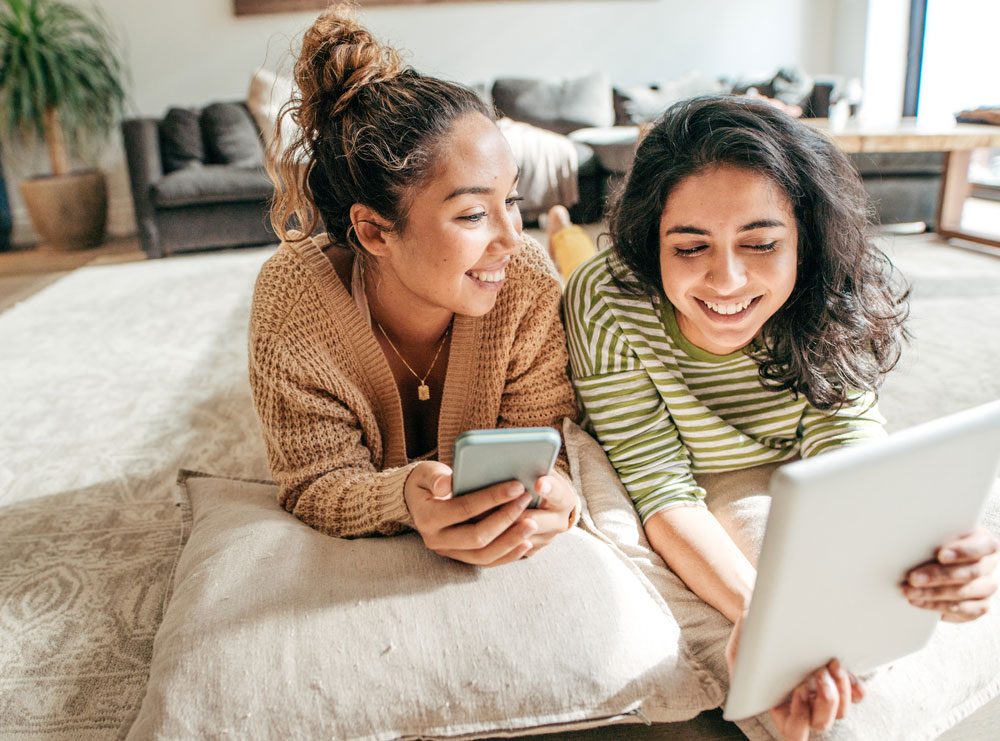 two girls using an iPad and phone
