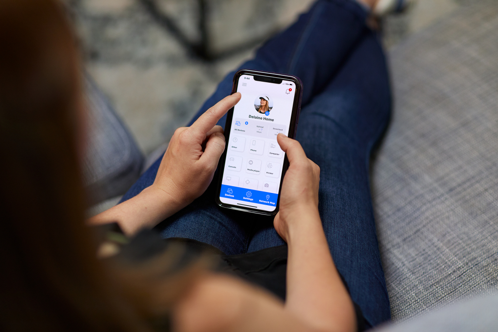 A top-down photo of a woman sitting on her couch, relaxed reviewing her family’s screen time on her phone.