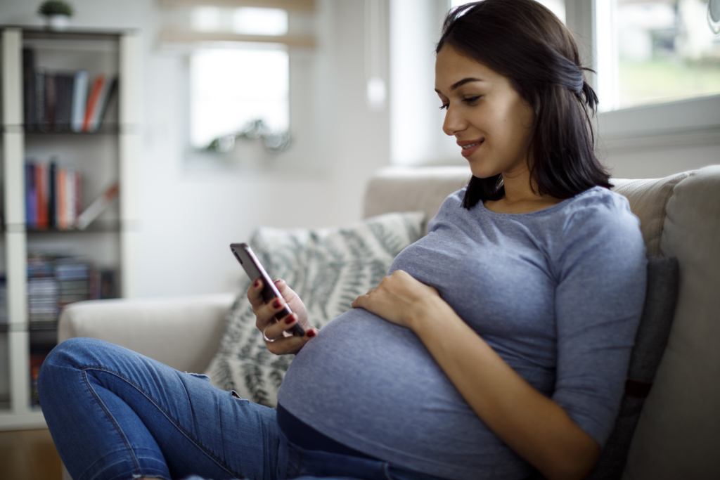 A mom looking relieved while checking her budget on her phone with a smile.
