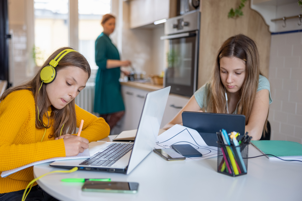 A mom cooking in the kitchen while two kids stream videos on tablets at the dining table.