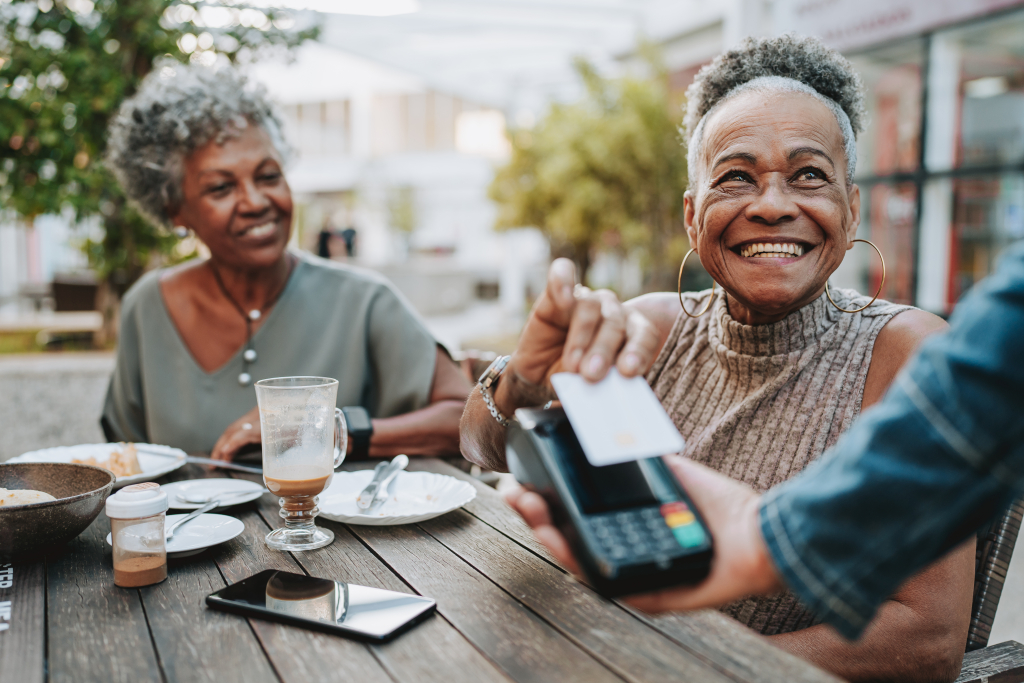 A happy woman paying for lunch with her friend via a wireless payment system.